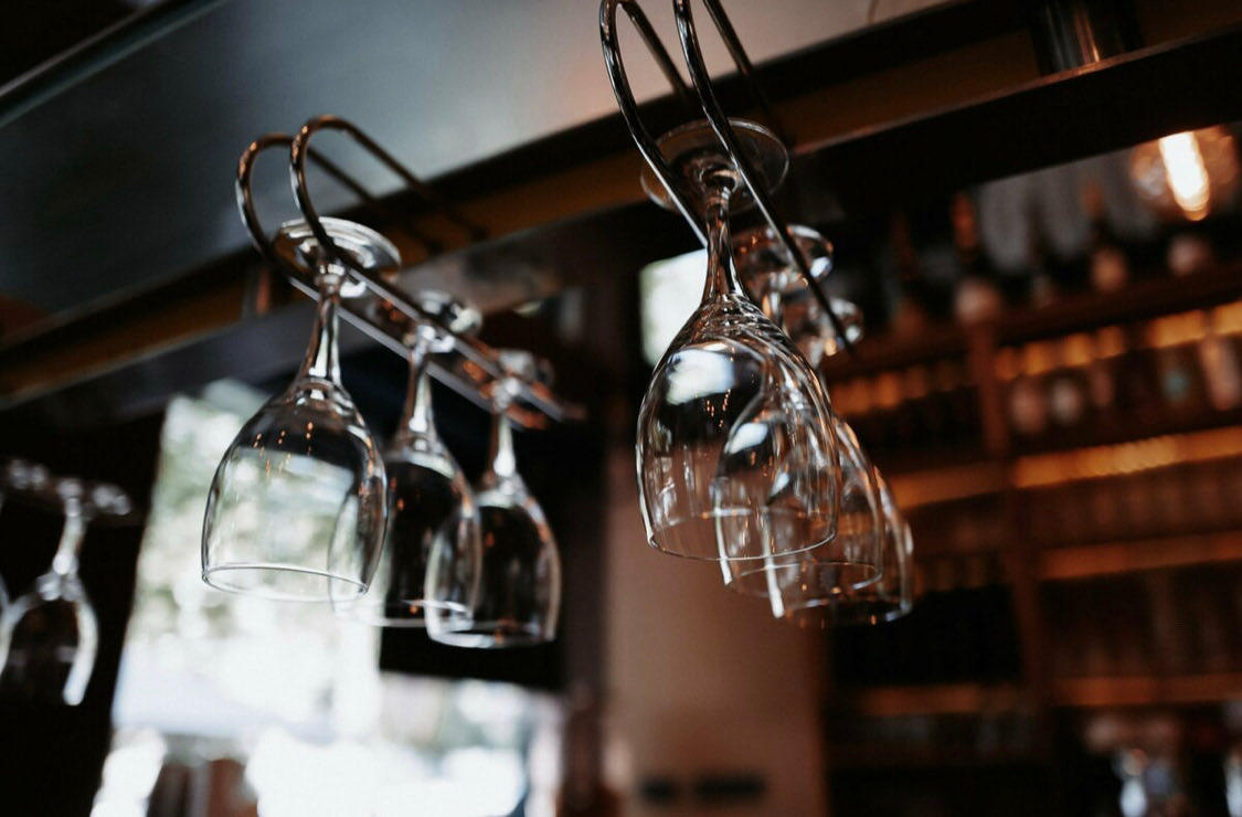 Kopfüber hängende Weingläser über der Bar, dahinter ein Weinregal im Halbdunkel