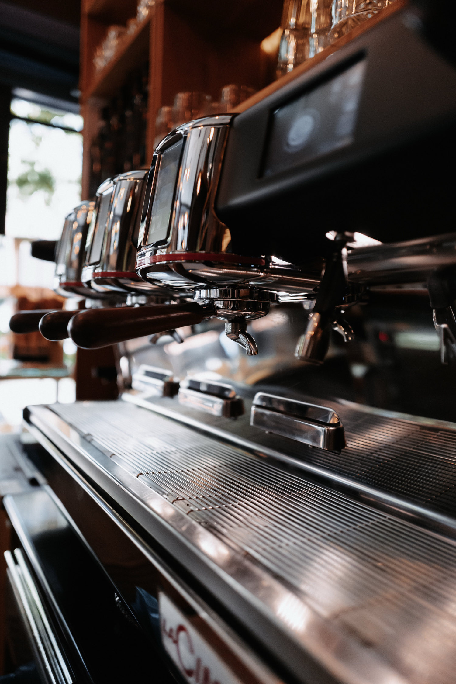 Siebträger-Espressomaschine aus Chrom von der Seite, dahinter das Regal hinter der Theke