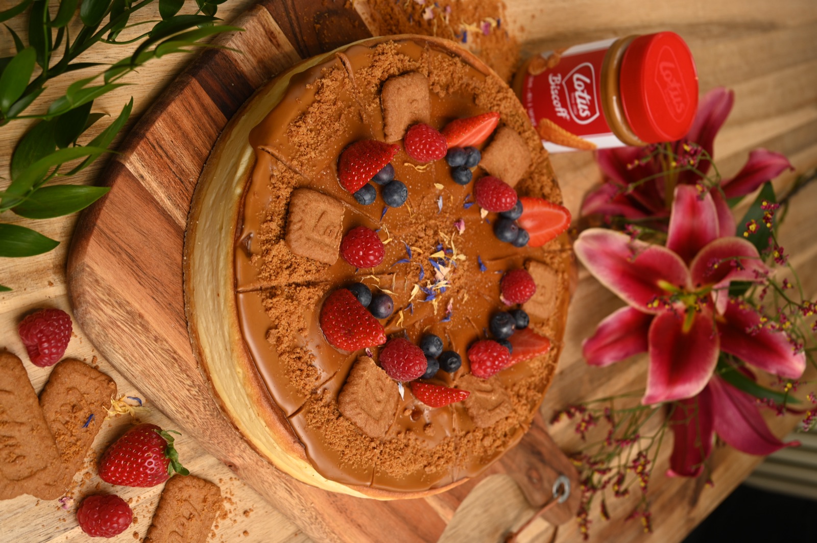 Torte mit Karamellcreme, Keksstücken, Erdbeeren und Heidelbeeren auf einer Holzplatte